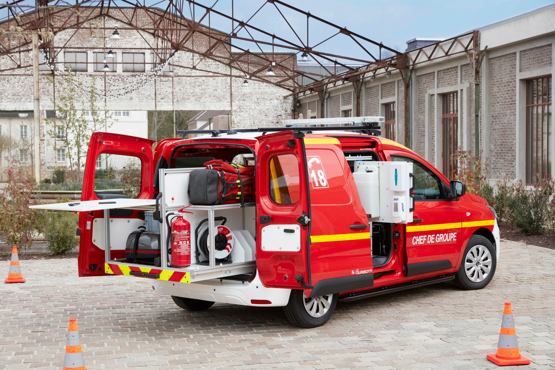 Renault Express Van modifikuotas specialiųjų tarnybų automobilis pastatytas šalia pilko pastato, pro atidarytas galines duris matoma gelbėjimo įranga