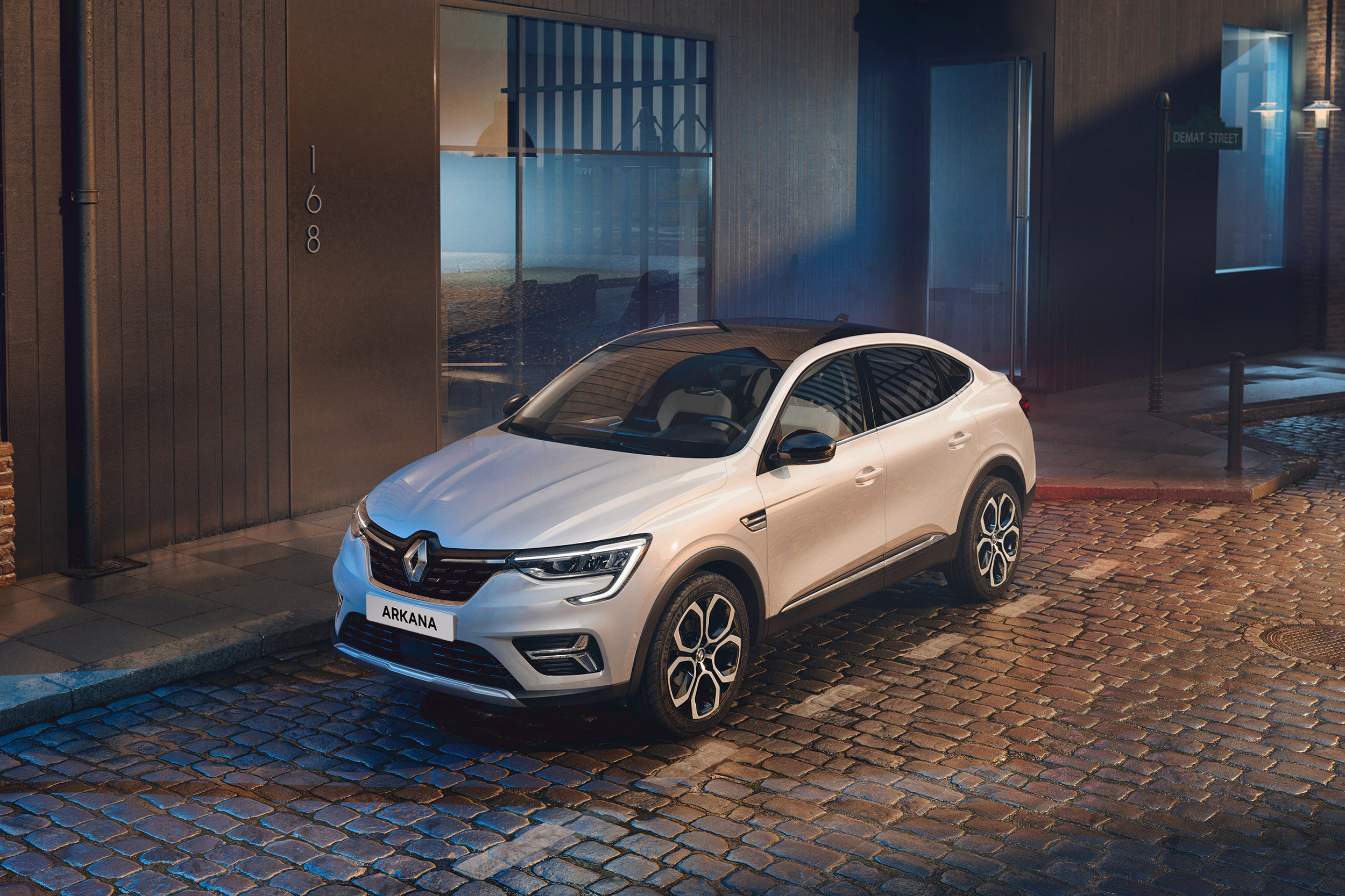 Baltas Renault ARKANA, pastatytas prie šaligatvio greta rudo pastato
