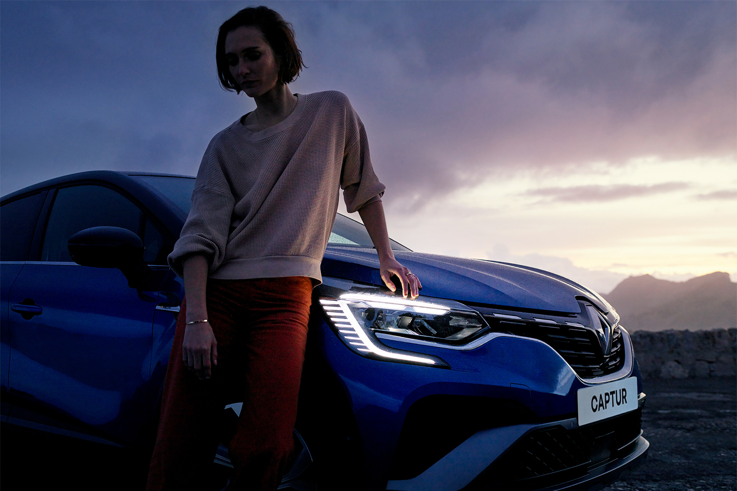 Moteris stovi atsirėmusi į mėlyno Renault CAPTUR R.S. Line variklio dangtį, šviečia priekinio Full LED žibinto dienos šviesos