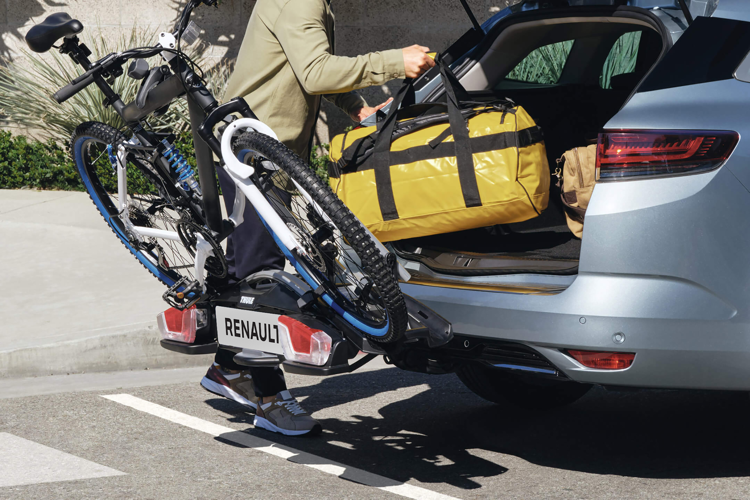 Vyras krauna krepšius į pilko Renault MEGANE bagažinę, prie vilkimo kablio pritvirtintas laikiklis su dviračiu